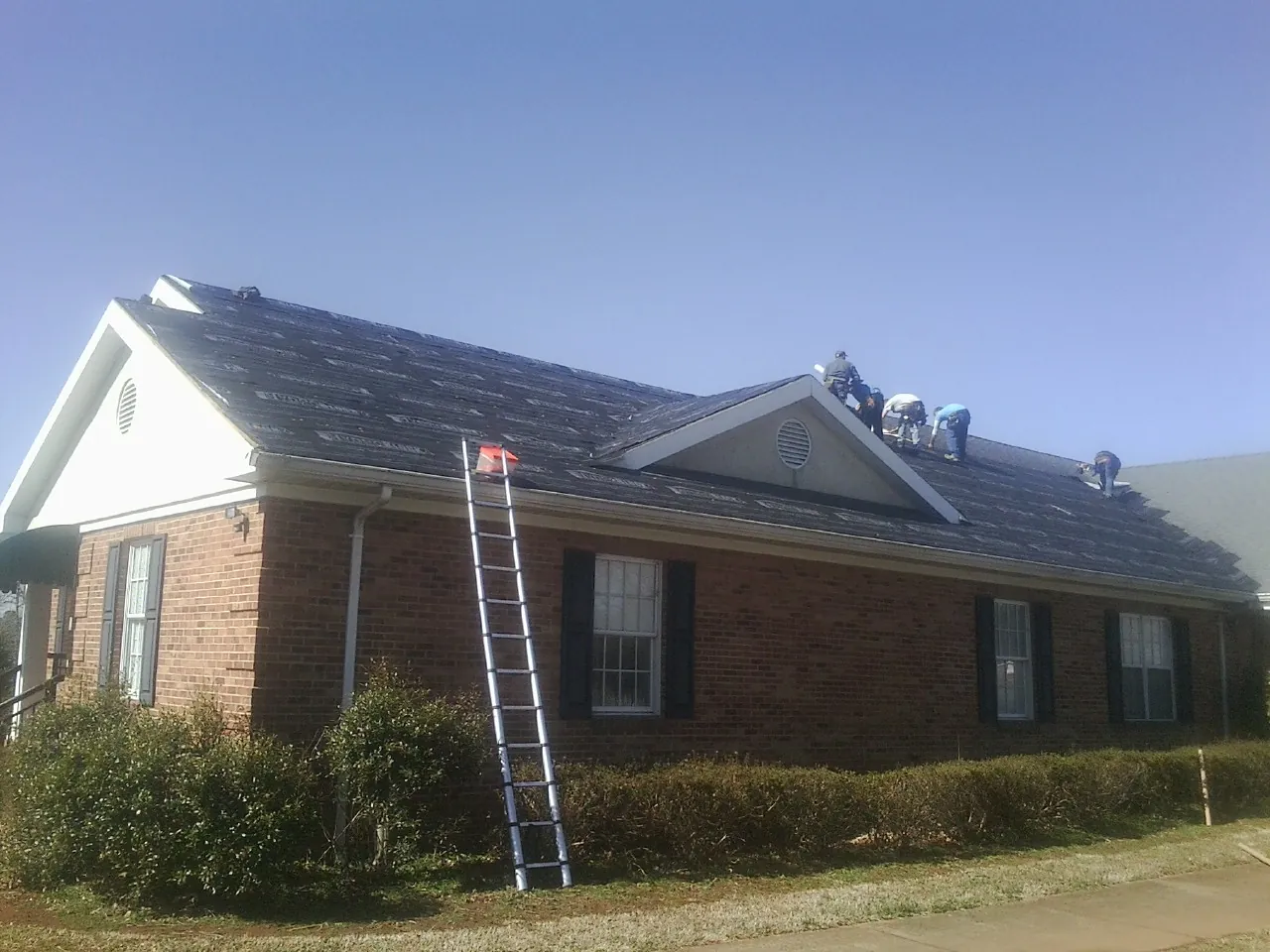 Crew tearing shingles off a brick ranch roof with a ladder set — Metal Roof Repair work by our crew in Contoocook