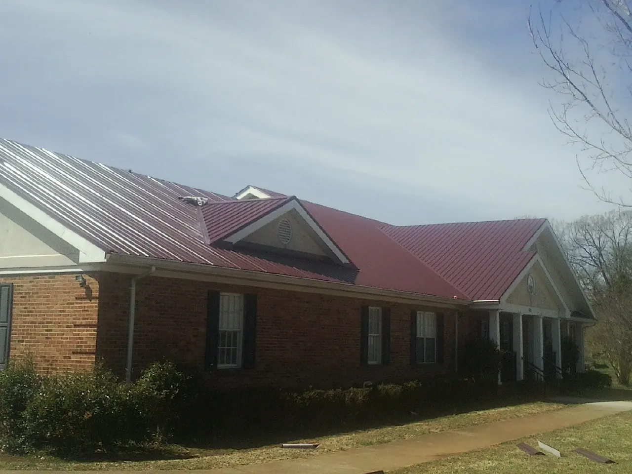 Red metal roof with gabled entries on a long brick building, from a Hail Damage Roof Repair job in Contoocook