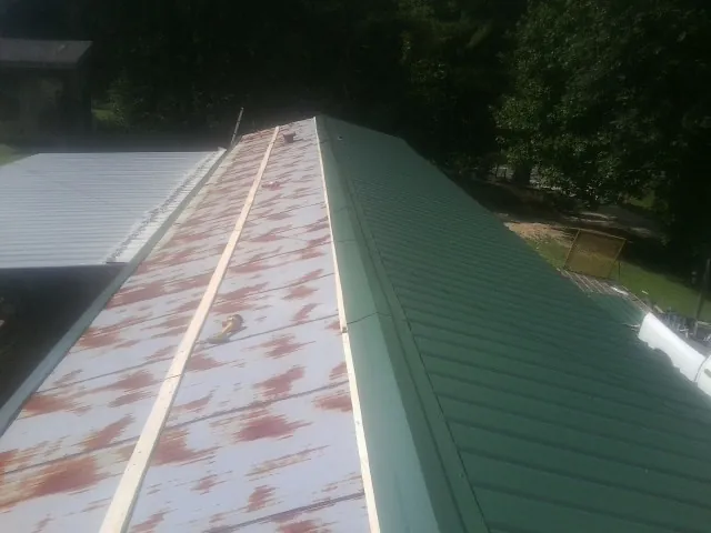 Old rusted panels beside newly installed green metal roofing — Wind Damage Roof Repair by Roofing Brothers in Contoocook