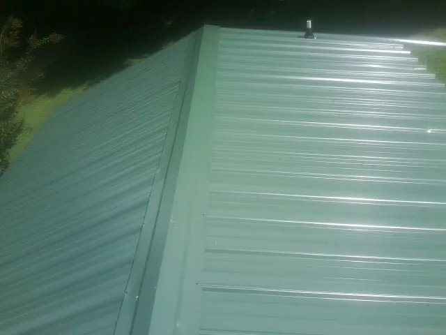 New green metal panels meeting at the ridge of a roof — Flat Roof Repair work by our crew in Contoocook