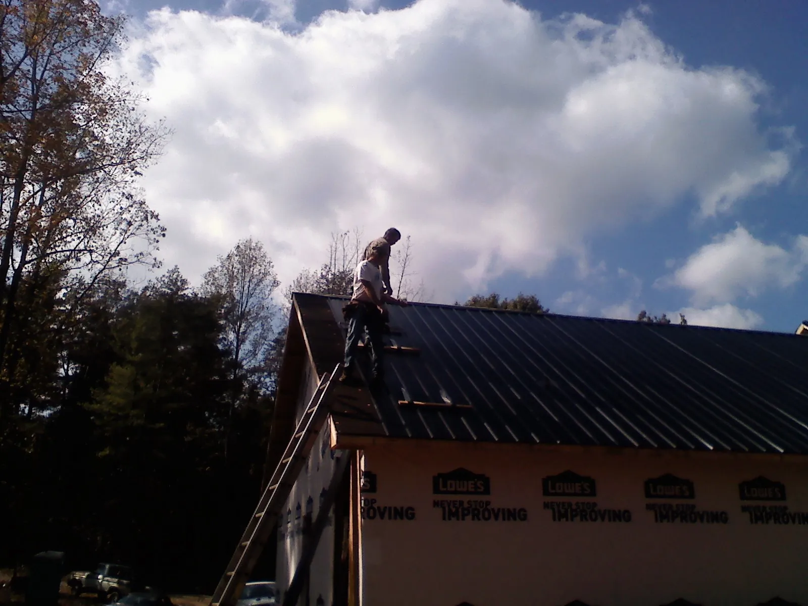 Roofer fastening dark metal panels high against a cloudy sky, from a Roof Inspection job in Contoocook