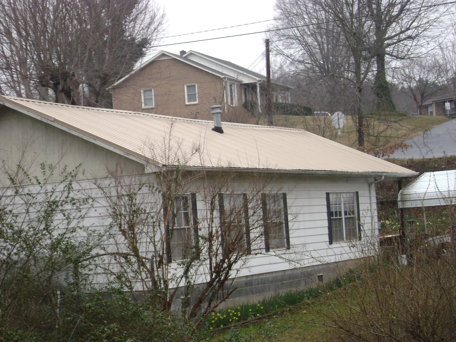 Tan metal roof on a white sided house set into a hillside — Commercial Roofing by Roofing Brothers in Contoocook